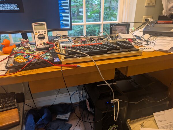 A desk with a lidless BBC Master, a multimeter, a sticker-covered laptop and a tangle of wires